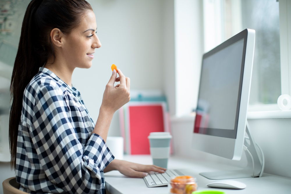 Female Worker In Office Having Healthy Snack Of Dried Apricot Fruit