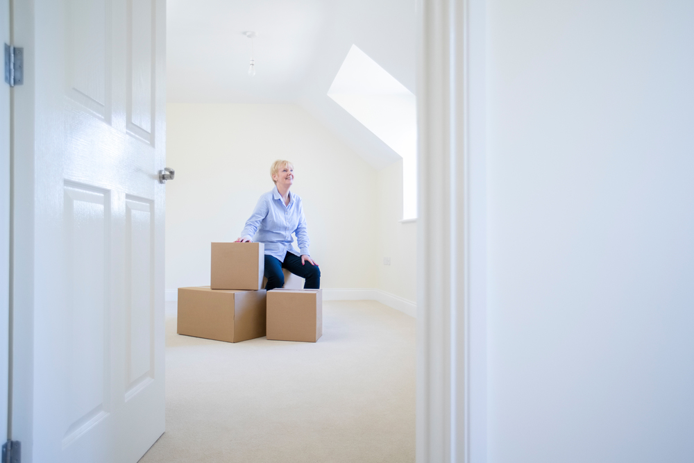 Senior Woman Downsizing In Retirement Sitting On Boxes In New Home On Moving Day