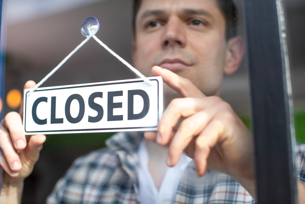 Small Business Owner With Serious Expression Putting Up Closed Sign During Recession Or Health Pandemic