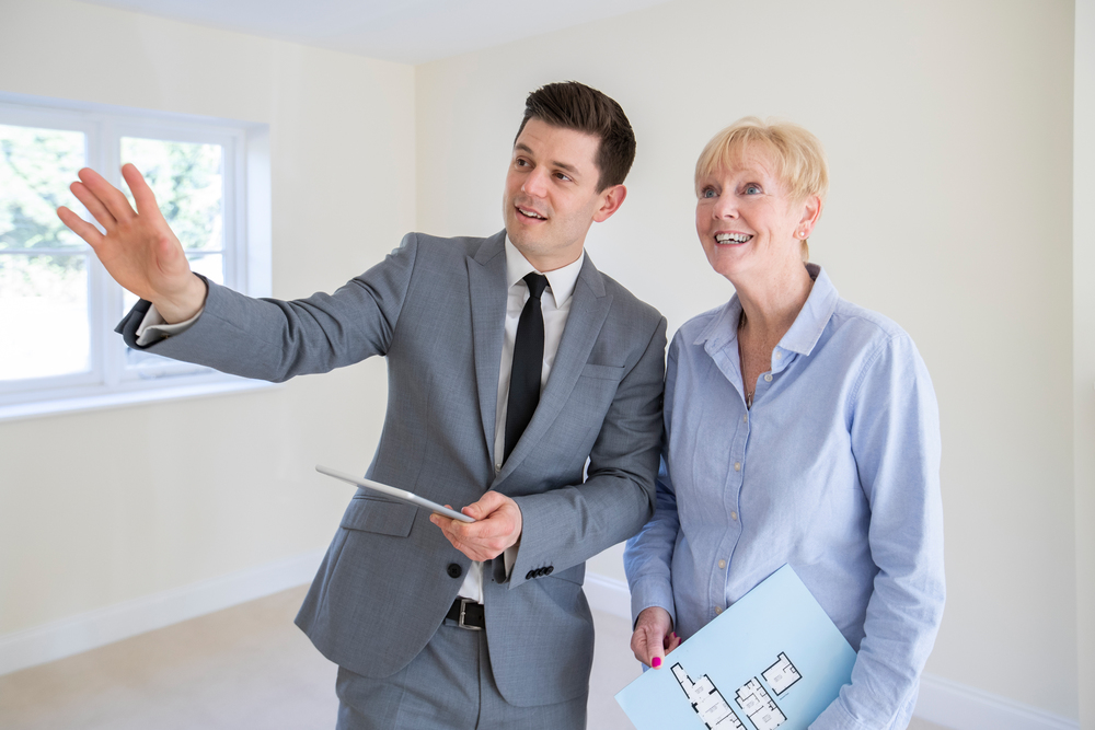 Realtor With Digital Tablet Showing Senior Woman Looking To Downsize Around Retirement Home