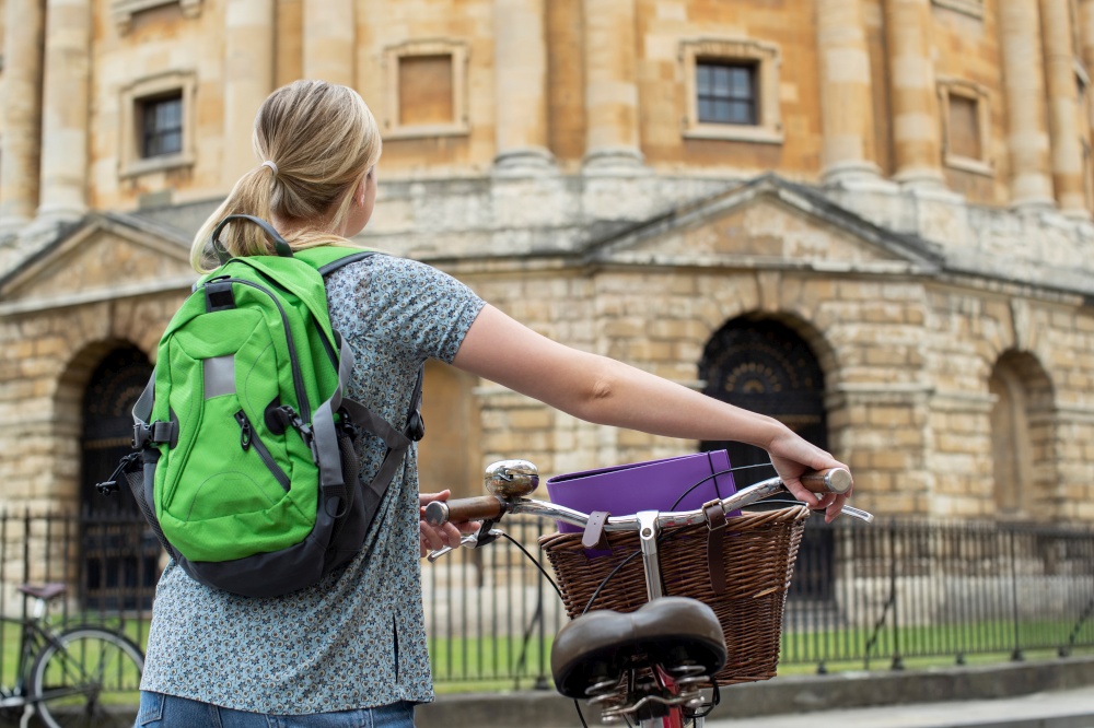 Rear View Of Female Student Riding Old Fashioned Bicycle Around Oxford University College Buildings By Radcliffe Camera In Radcliffe Square UK