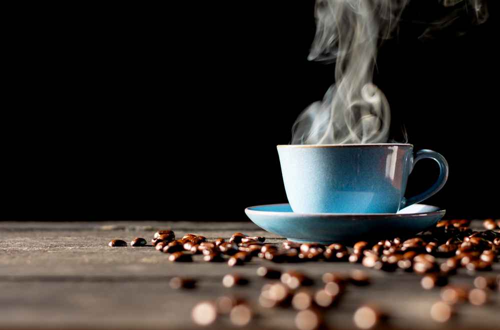 Hot coffee in blue cup and roasted coffee beans placed on a black wooden table.