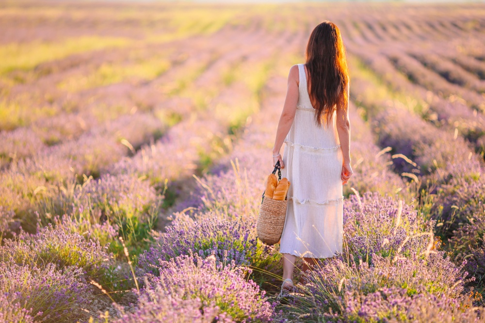 Beautiful young woman on purple flower lavender field. Woman in lavender flowers field at sunset in white dress and hat