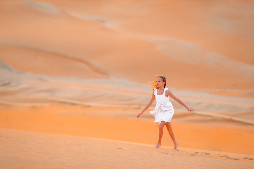Beautiful girl in white dress on vacation in dunes in beautiful desert. Girl among dunes in desert in United Arab Emirates