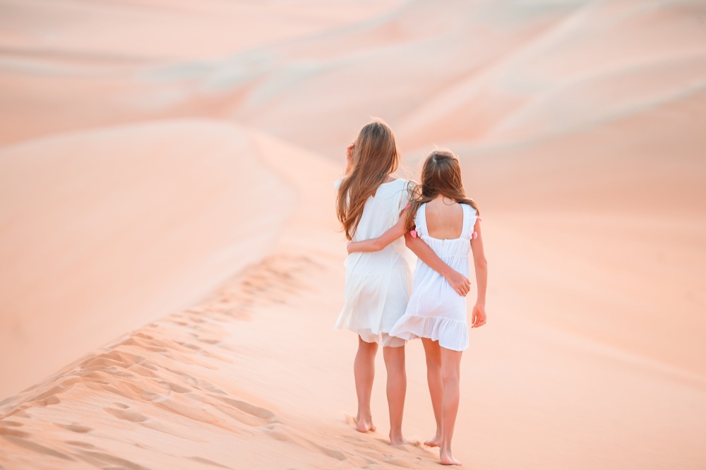 Little beautiful girls at dunes in most big sand desert in the world. Girls among dunes in big desert in Emirates