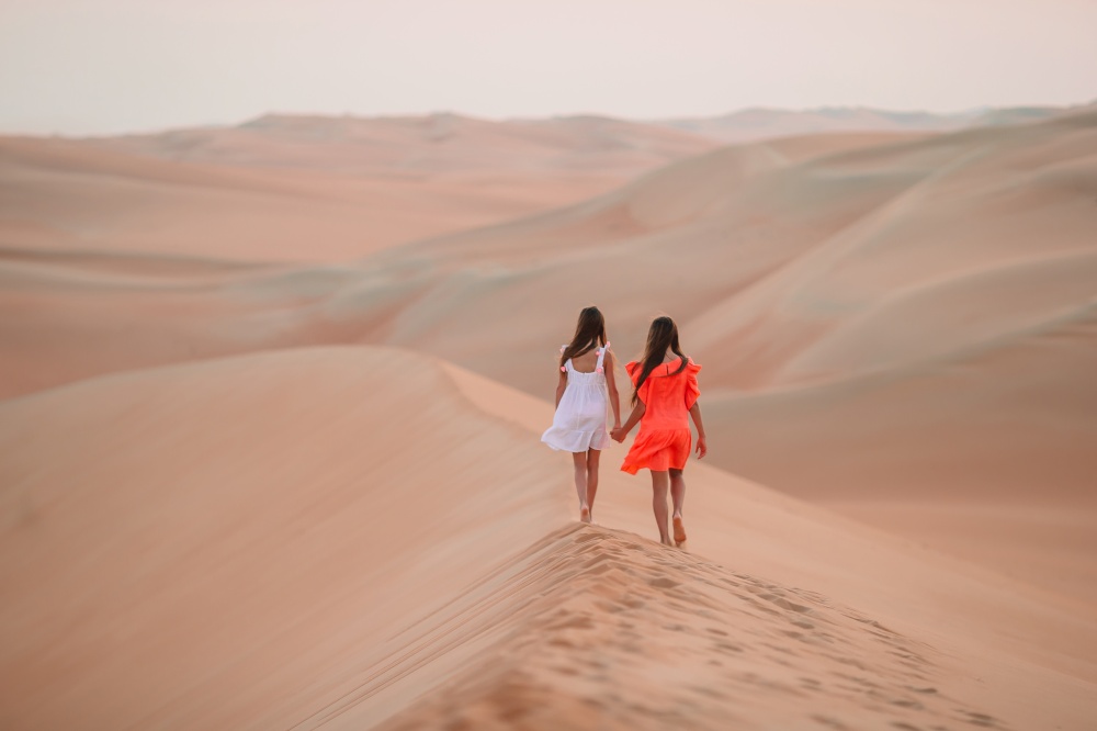 Little cute girls at dunes in desert at sunset. Girls among dunes in Rub al-Khali desert in United Arab Emirates