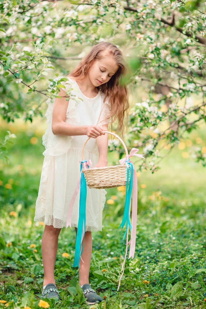 Cute little girl with long hair in blooming apple tree garden searching Easter eggs. Adorable little girl in blooming apple garden on beautiful spring day