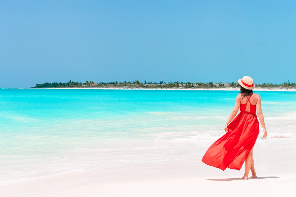 Beautiful woman on tropical seashore. Young girl in beautiful red dress and straw hat on the beach. Young girl in beautiful red dress background the sea