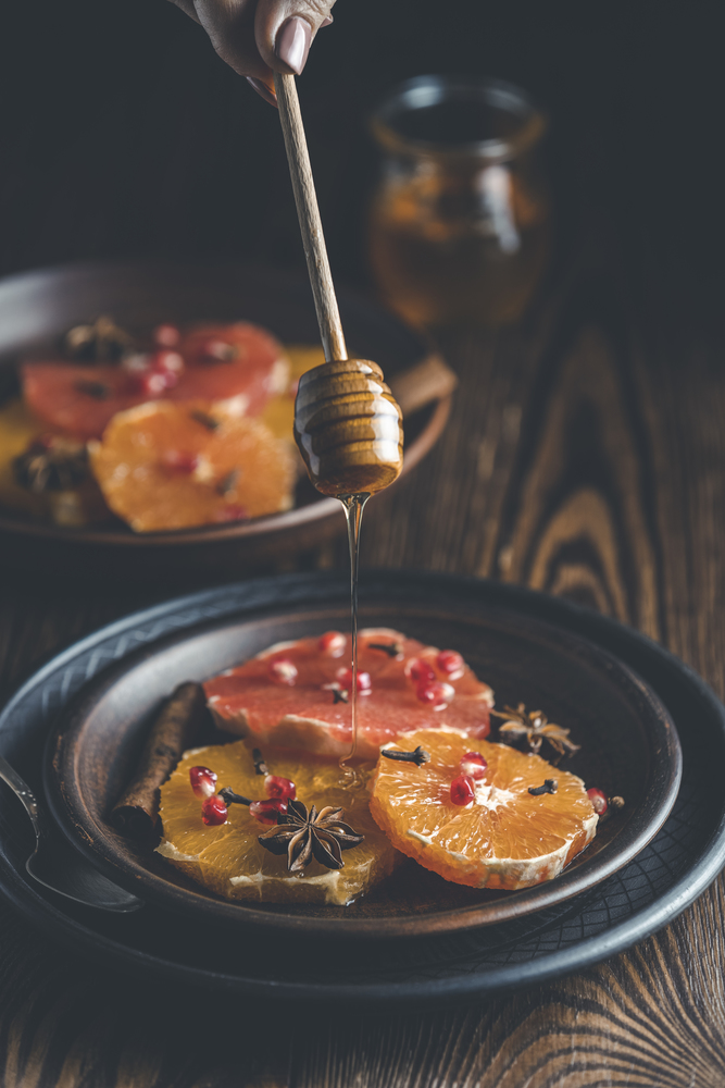 Orange dessert with wine honey or maple syrup and ginger spice, decorated pomegranate berries. Wonderfully sweet, rich and fresh food. Dark rustic background, copy space for you text.
