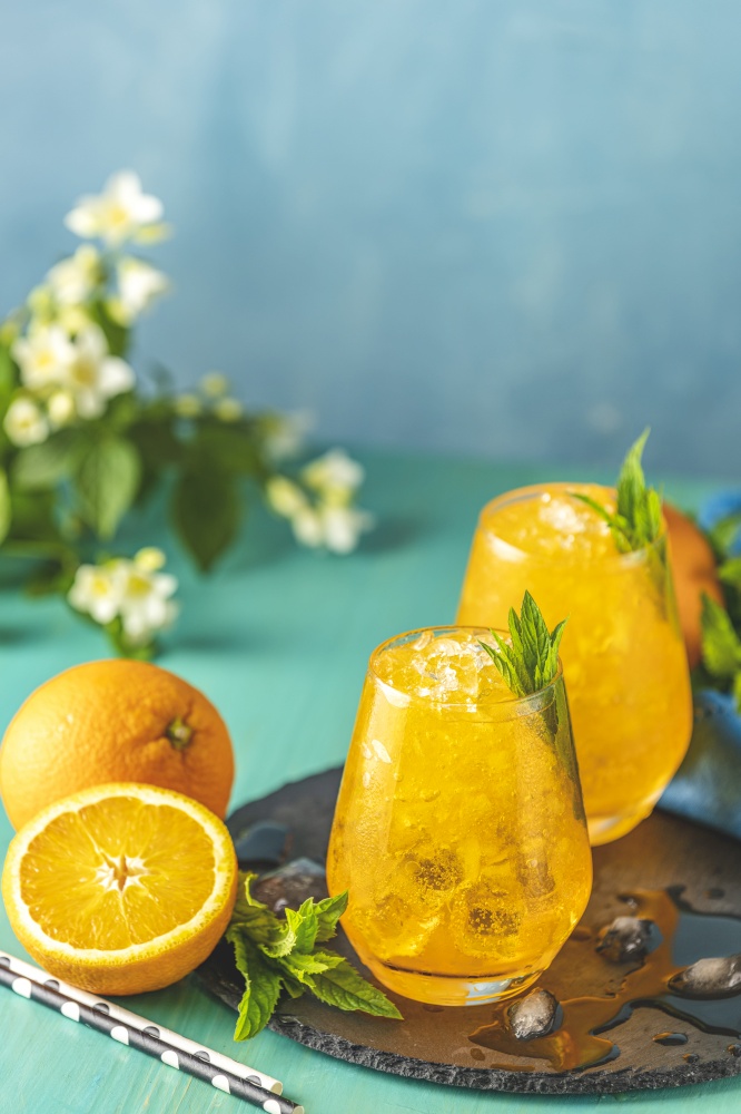 Orange drink with ice. Two glass of orange ice drink with fresh mint on wooden turquoise table surface. Alcoholic non-alcoholic drink-beverage