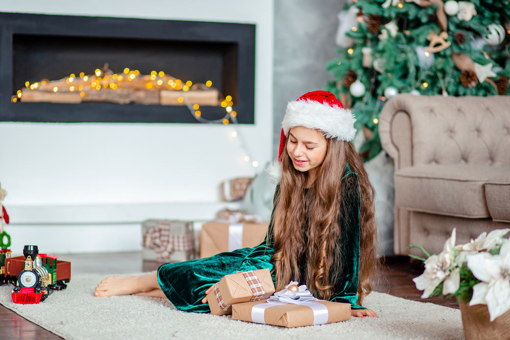 Little girl Santa Claus hat with gifts under Christmas tree sitting by the fireplace, unpacks gifts. Merry Christmas.. Little girl Santa Claus hat with gifts under Christmas tree sitting by the fireplace, unpacks gifts.