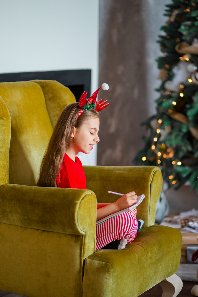 A cute girl in a Santa hat writes a letter to Santa near the Christmas tree. Happy childhood, a time for fulfilling desires. Merry Christmas.. A cute girl in a Santa hat writes a letter to Santa near the Christmas tree. Happy childhood, a time for fulfilling desires.