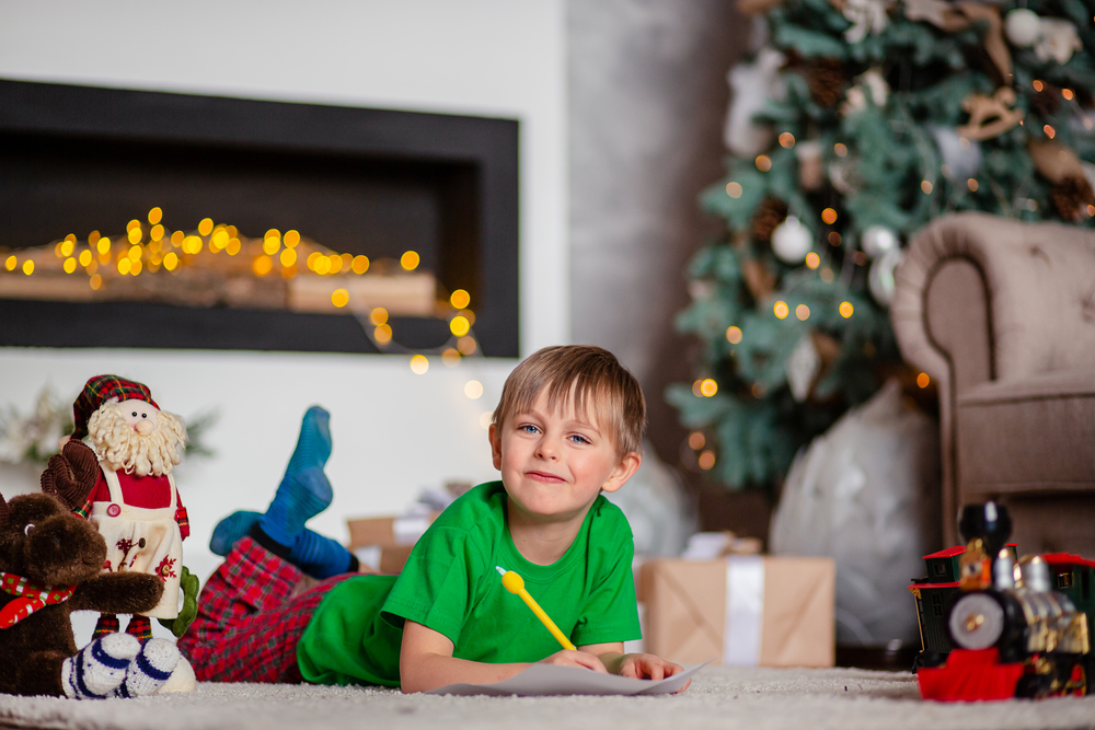 Cheerful boy is a letter to Santa, near the Christmas tree. Happy childhood, time for fulfilling wishes. Merry Christmas.. Cheerful boy is a letter to Santa, near the Christmas tree. Happy childhood, time for fulfilling wishes.