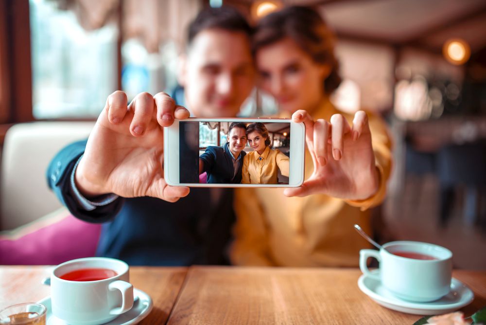Love couple makes selfie on phone camera in restaurant. Man and woman dating celebration. Love couple makes selfie on camera in restaurant