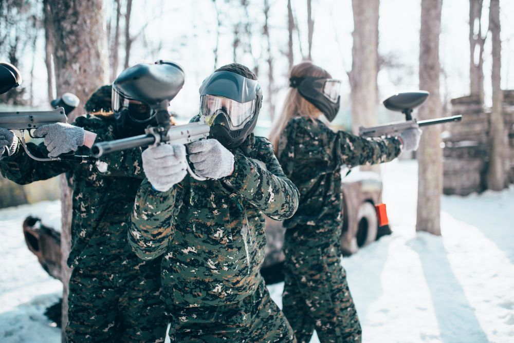 Paintball players in uniform and masks poses with marker guns in hands after winter forest battle. Extreme sport game. Paintball players in uniform and masks poses
