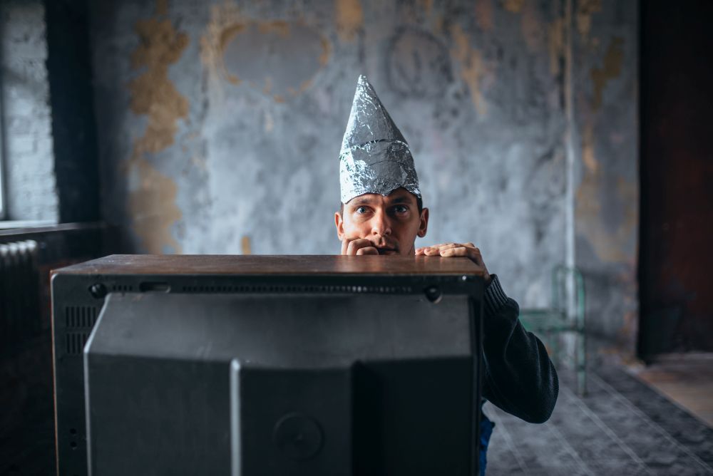 Afraid man in aluminum foil cap watch TV, mind protection, paranoia concept. UFO, conspiracy theory, telepathy phobia. Afraid man in aluminum foil cap watch TV, UFO