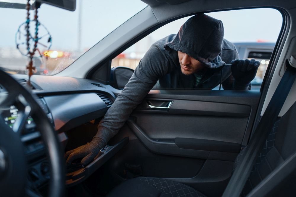 Car robber steals women&rsquo;s handbag, criminal lifestyle, stealing. Hooded male bandit opening vehicle on parking. Auto robbery. Car robber steals women&rsquo;s handbag, stealing