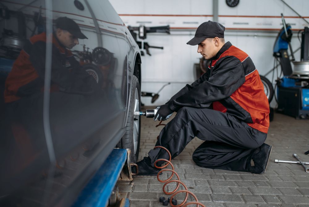 Mechanic with pneumatic wrench unscrews the wheel in tire service. Man repairs car tyre in garage, automobile inspection in workshop. Mechanic with pneumatic wrench unscrews the wheel