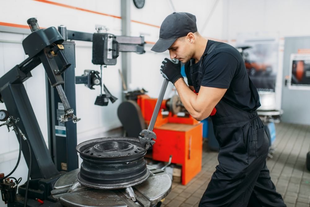 Mechanic fixing broken wheel, tire repairing service. Man repairs car tyre in garage, professional automobile inspection in workshop