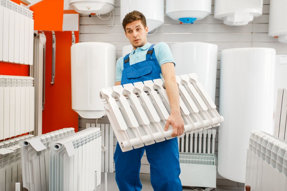 Plumber in uniform holds water heating radiator at showcase in plumbering store. Man buying sanitary engineering in shop