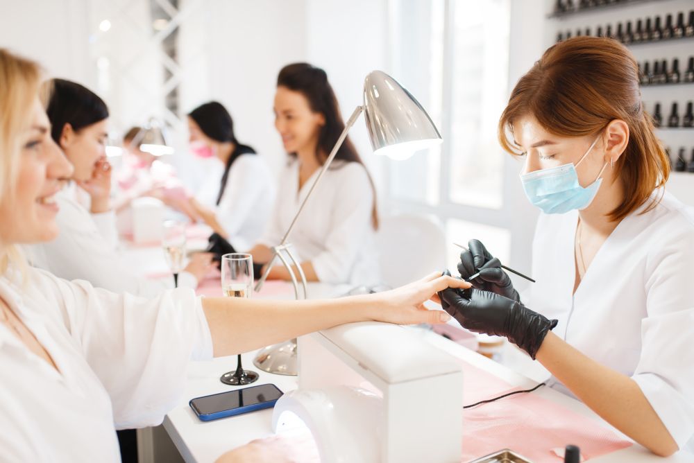 Group of women relax on manicure procedure in beauty salon. Professional beautician and female customers, nail care in spa studio, fingernail treatment. Group of women on manicure procedure, beauty salon