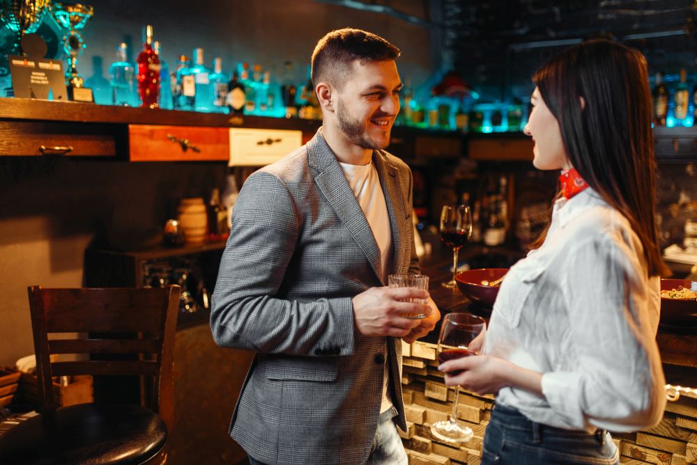 Love couple with alcoholic beverages talking at bar counter, romantic evening of man and woman. Lovers leisures in pub, husband and wife relaxing together in nightclub