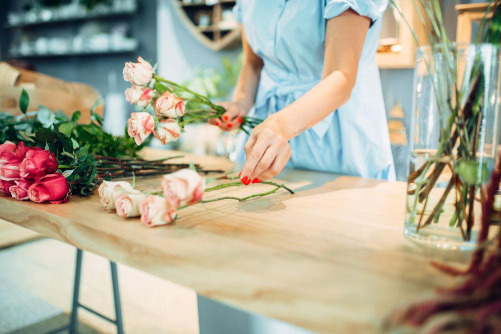 Female florist makes rose composition on the table in flower shop. Floral artist making bouquet at the workplace