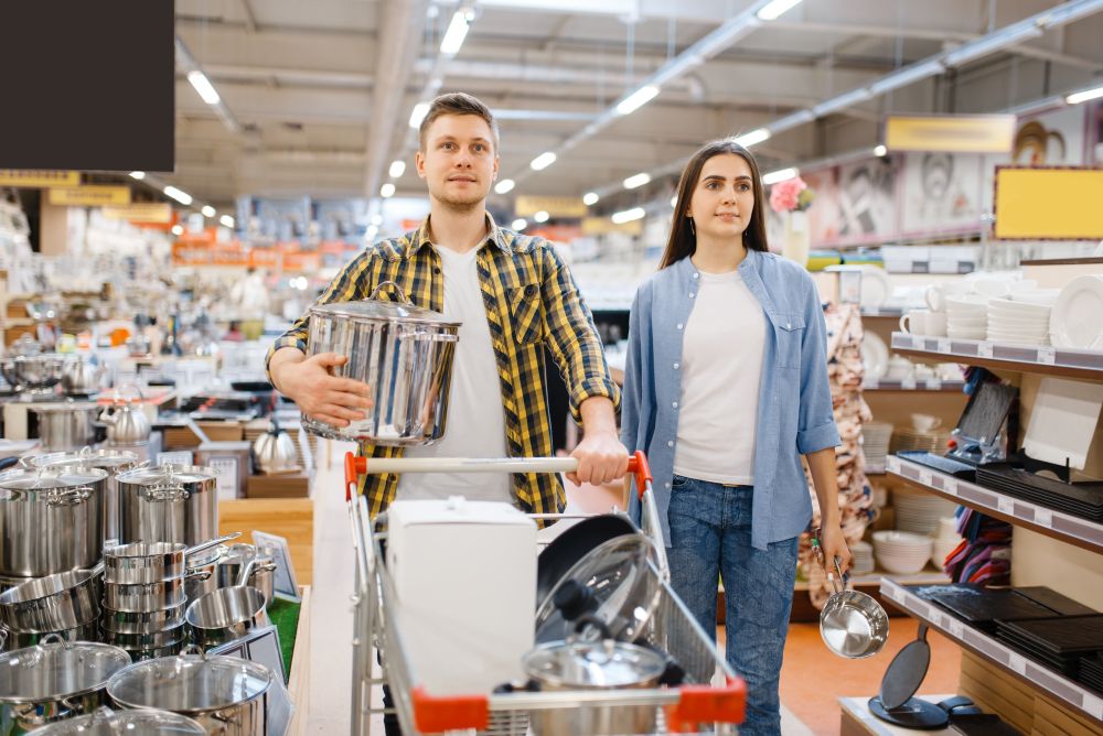 Young couple with cart in houseware store. Man and woman buying home goods in market, family in kitchenware supply shop. Young couple with cart in houseware store