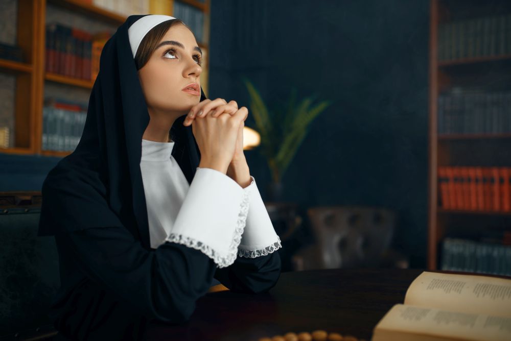 Young nun in a cassock prays crossed her arms. The sister in the monastery, religion and faith, religious people. Young nun in a cassock prays crossed her arms