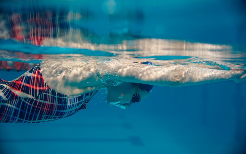 Female swimmer in swimsuit, cap and glasses swimming in pool, underwater view. The woman holds her breath in the water, breath-hold technique exercise. Female swimmer swimming in pool, underwater view