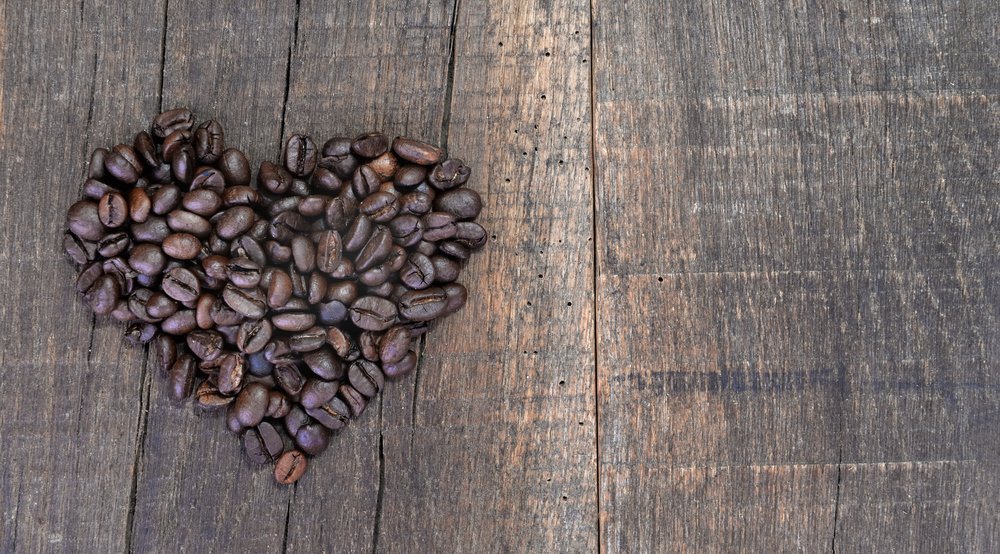 heart shaped making with beans of coffee arranged on a rustic plank with copy space on the right