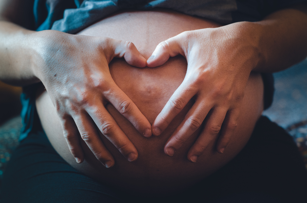 Pregnant woman with her hands and fingers making a heart on her belly, where her baby is.. Pregnant hands making a heart on her belly