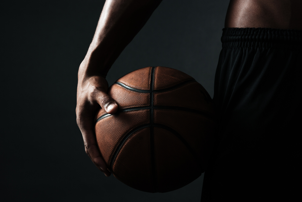 Cropped photo of basketball player holding ball, over black background