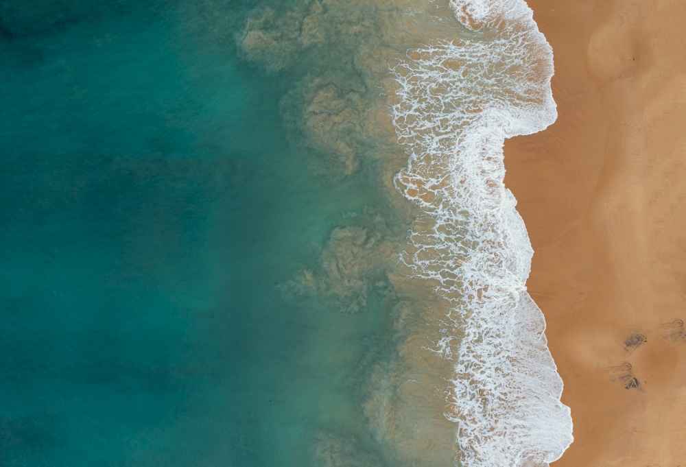 An aerial shot of the beautiful ocean waves meeting the sands on the beach. Aerial shot of the beautiful ocean waves meeting the sands on the beach