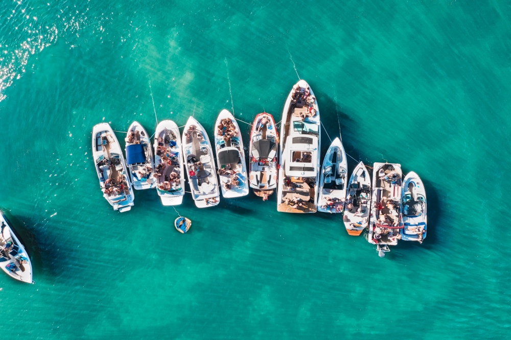 An overhead aerial drone shot of different sized boats docked close to each other near the pier. Overhead aerial drone shot of different sized boats docked close to each other near the pier