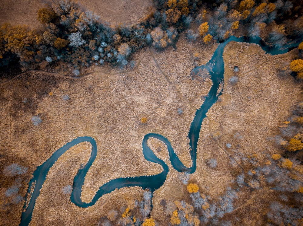 An aerial shot of a river in the middle of a dry grassy field with trees great for background or a blog. Aerial shot of a river in the middle of a dry grassy field with trees great for background