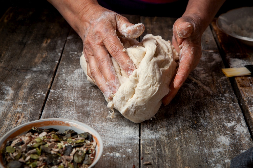 Woman making dough on wooden table close-up.