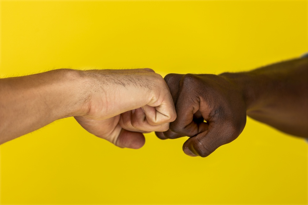 foreground european and afroamerican hand to hand clenched into fists on the yellow background