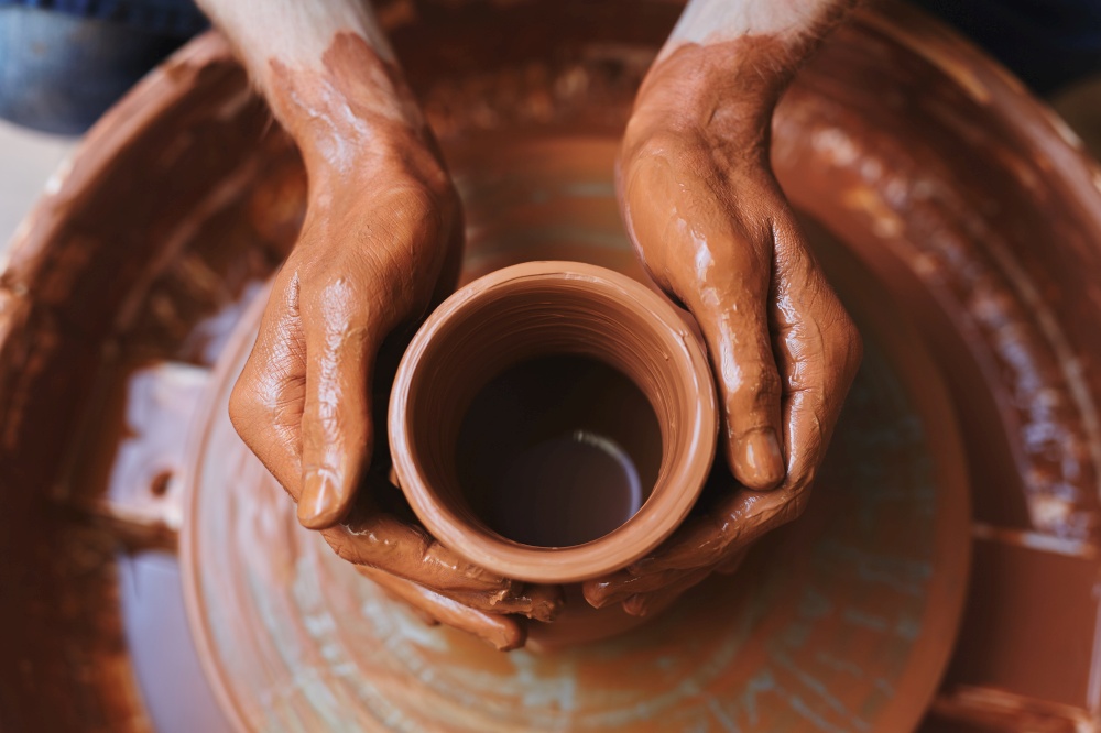 Dirty hands of potter on rotating clay jug. Unfinished jug