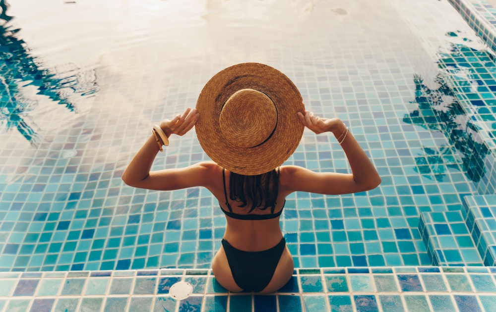 The woman in the hat relaxes on an inflatable circle in the form of a donut in the blue pool. The view from the top . The concept of summer pastime .. A woman in a hat relaxes on an inflatable circle in the pool.