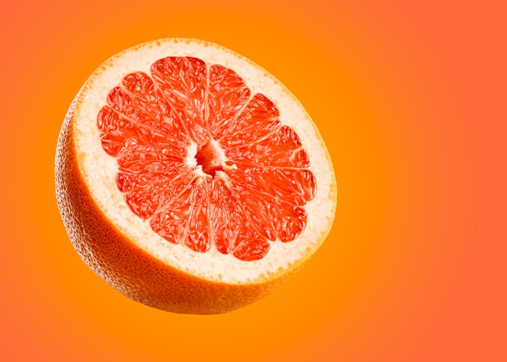 Grapefruit closeup isolated on orange background. Very detailed macro shoot with subject on left and copy space on right.. Grapefruit closeup isolated on orange background.