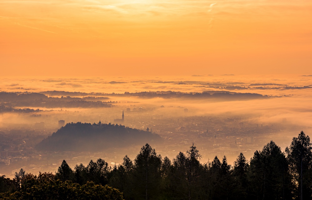 Graz city covered if fog on autumn morning during sunset. View from Plaubutsch hill surrounding city.. Graz city covered if fog on autumn morning during sunset.
