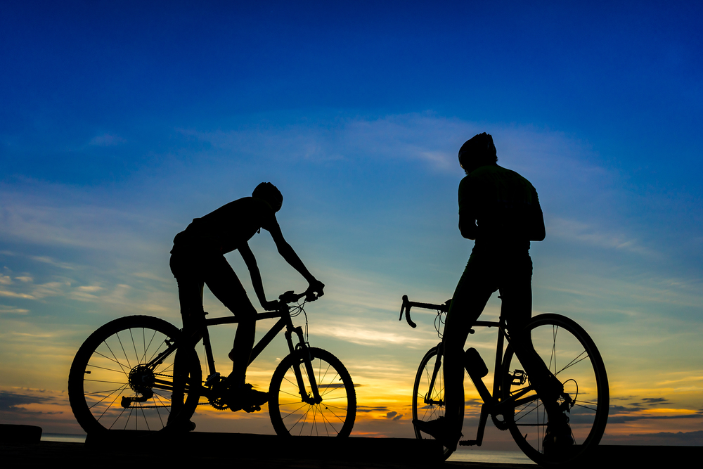 Two Cyclists with their bicycles at the beach, sunset scene.