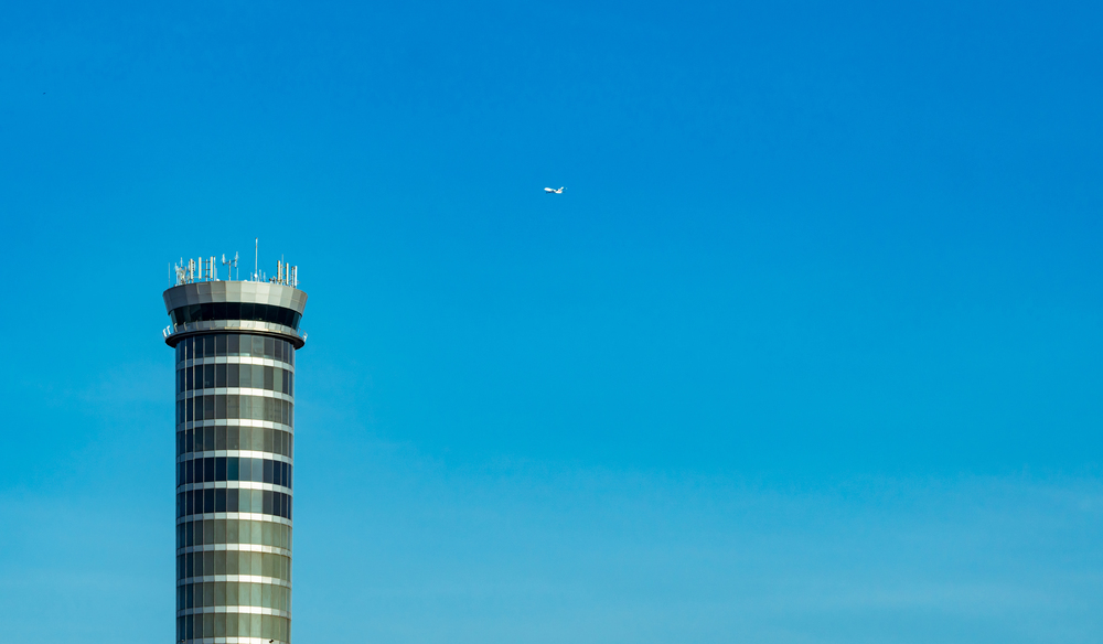 Air traffic control tower in the airport with international flight plane flying on clear blue sky. Airport traffic control tower for control airspace by radar. Aviation technology. Flight management.