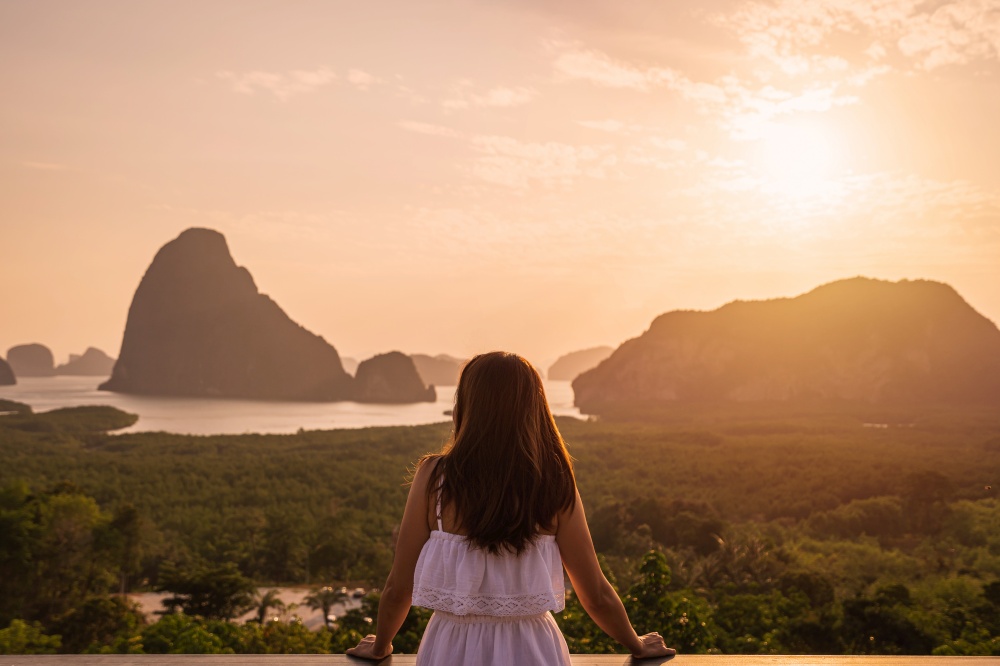 Young woman traveler looking at sunrise over the mountain at samet nang she, Thailand