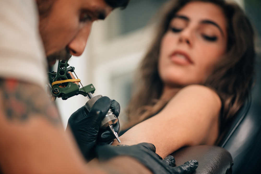 Tattoo artist creating a tattoo on a girl&quot;s arm. Focus on tattoo machine