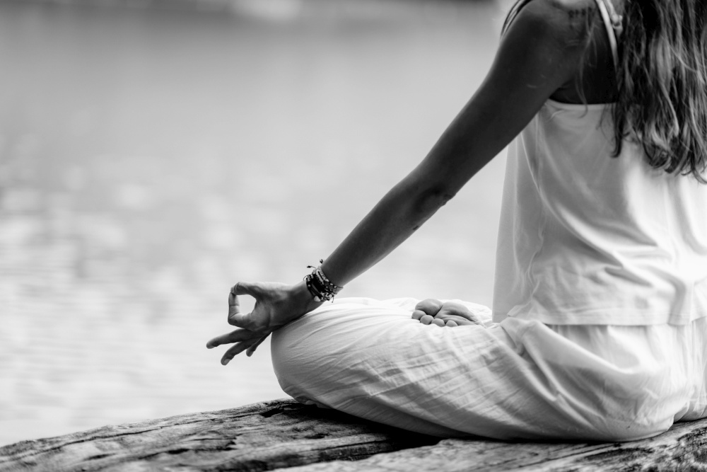 Close up image of woman&rsquo;s hands in lotus position by the lake
