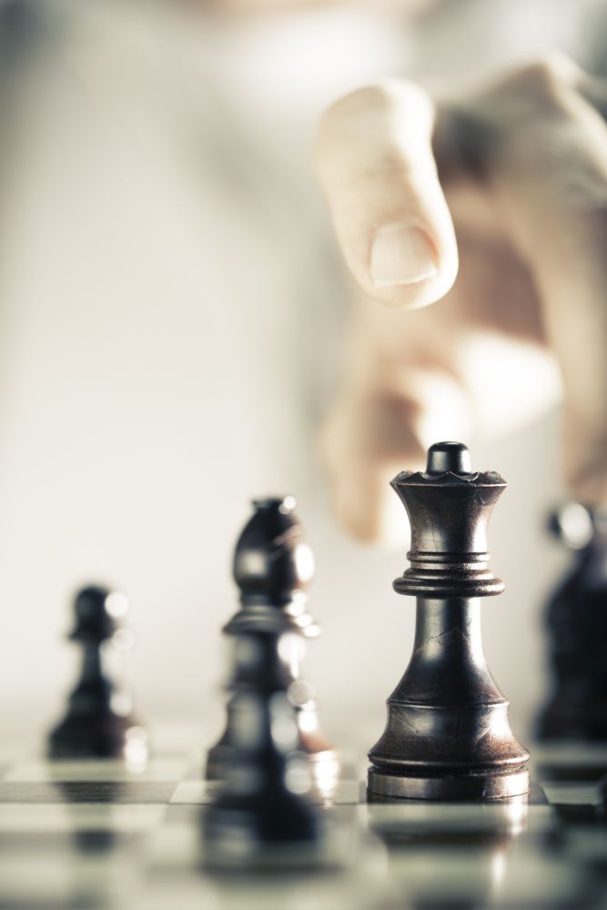 Vertical Image of a chess game with focus on the queen and a blurry hand at the background, Copy space on the left side. Concept of strategic business or risk management.. Chess Game Background
