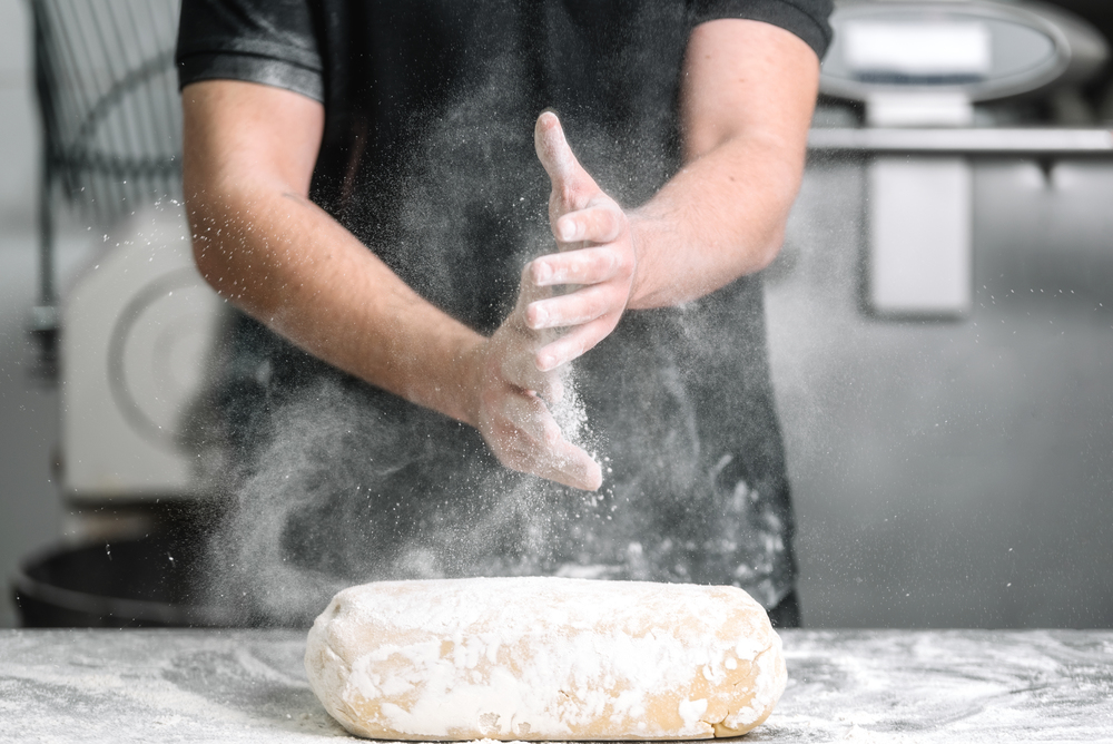 Baker claping hands with flour in restaurant kitchen .. Baker claping hands with flour in restaurant kitchen.