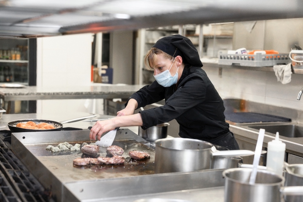 Woman Chef in protective face mask prepare food in the kitchen of a restaurant or hotel. Coronavirus prevention concept. High quality photo. Woman Chef in protective face mask prepare food in the kitchen of a restaurant or hotel. Coronavirus prevention concept.